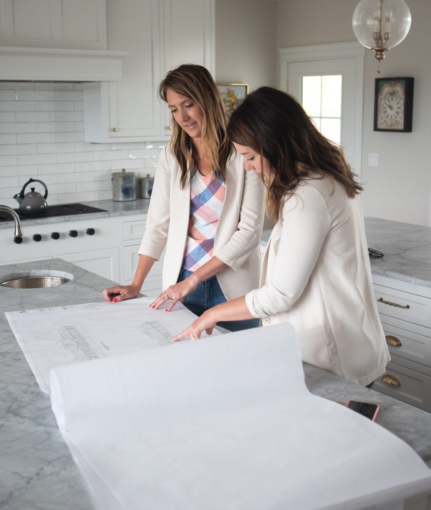 Two sisters read over construction documents in kitchen.