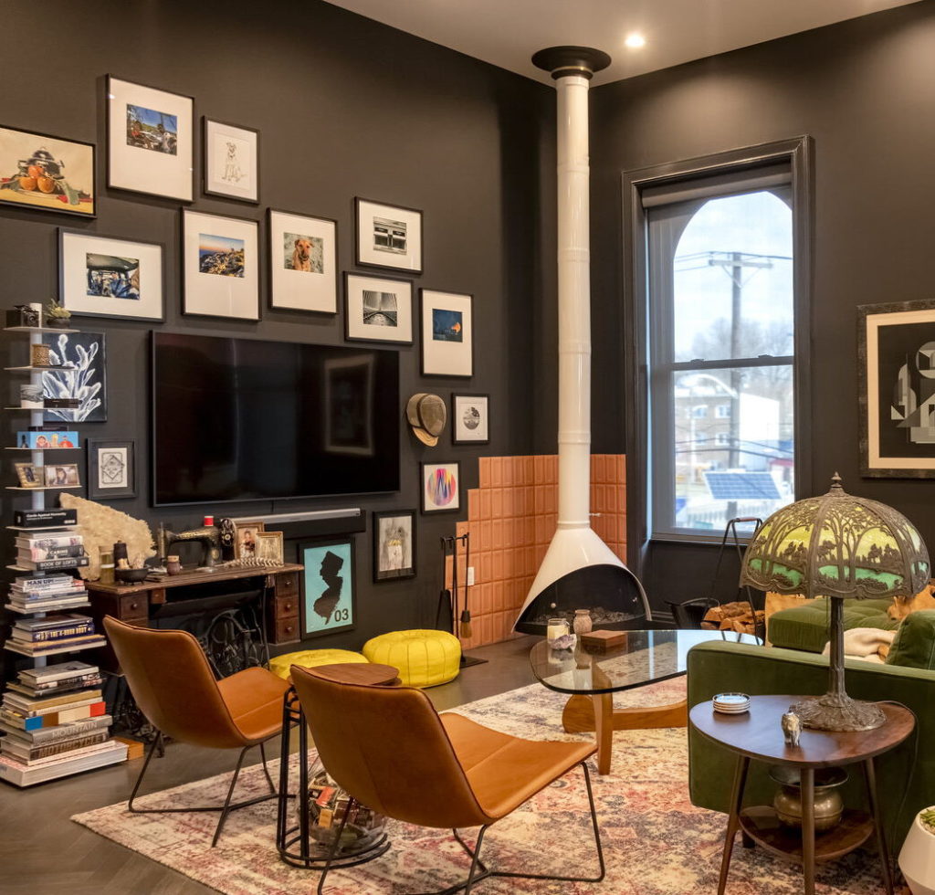 Image of a living room with black walls, a custom fireplace and a gallery wall.