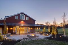 The exterior of the red party barn in the evening. A stone accent wall surrounds a fire pit and provides plenty of seating.