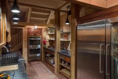 A view of the rustic kitchen in the party barn with wood cabinetry, open shelving, and an industrial size stainless steel refrigerator.
