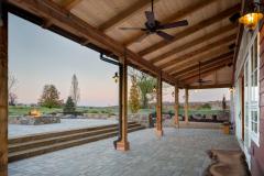 The exterior of the red party barn's covered patio in the evening. A stone accent wall surrounds a fire pit and provides plenty of seating.
